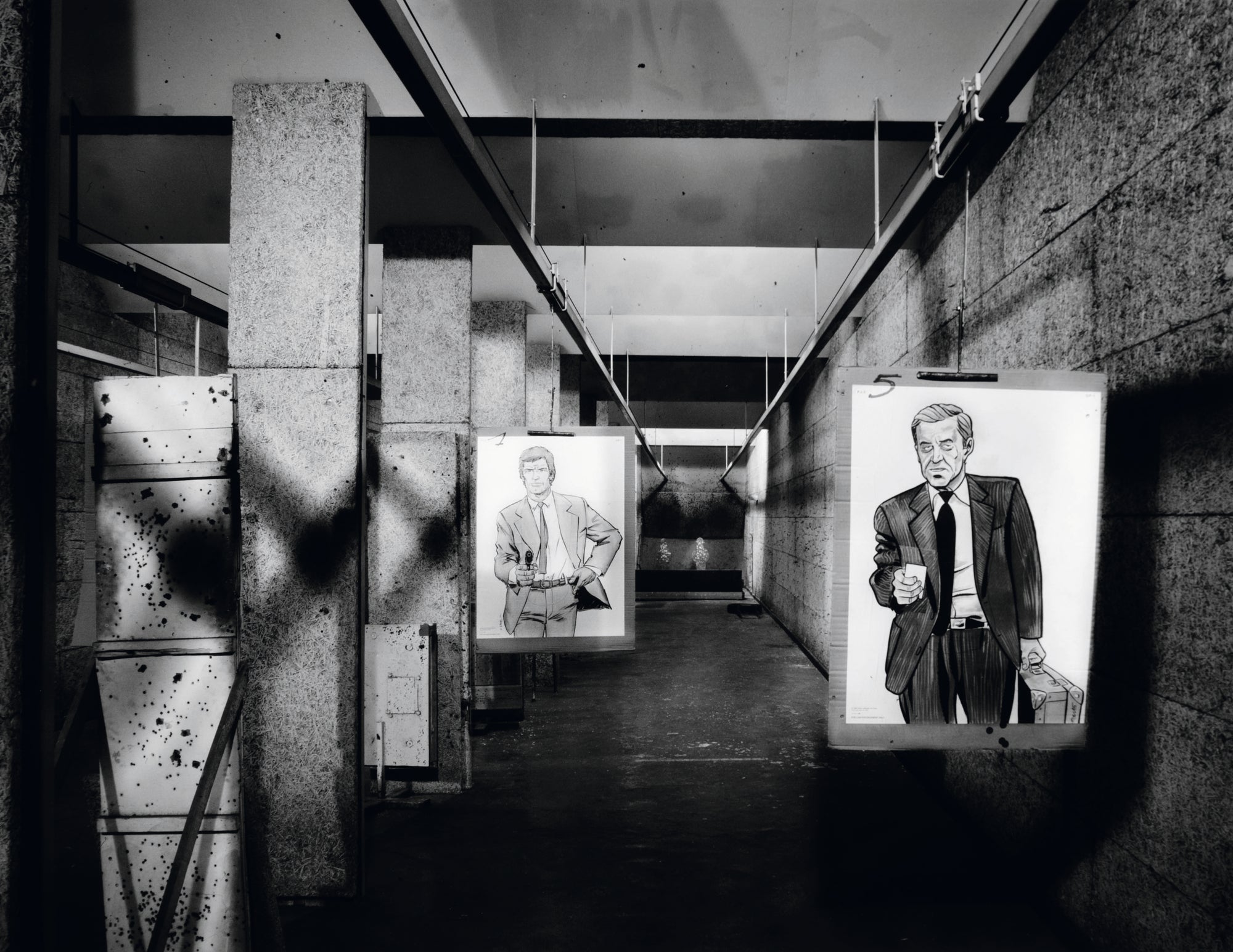 Black and white photograph of a long corridor with two large framed portraits mounted on the walls. The left portrait shows a man in a suit holding a briefcase, and the right portrait shows a man in a suit holding a cigar.