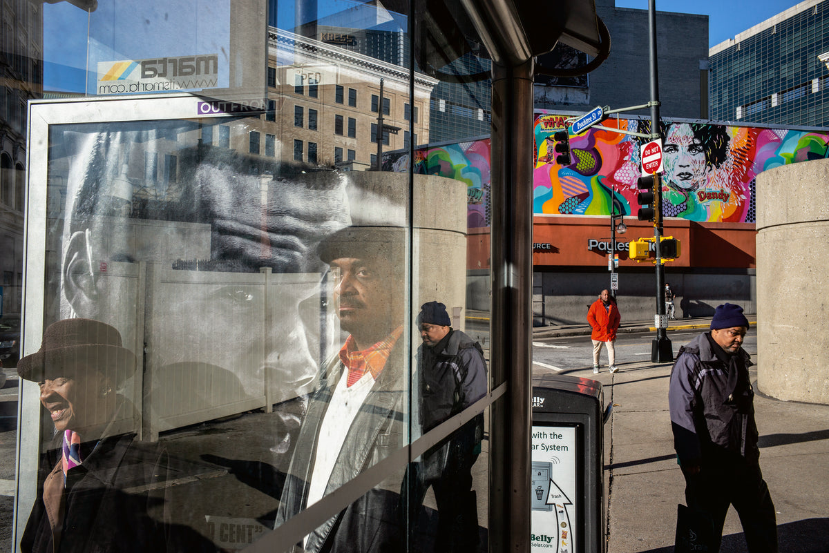 People waiting at a bus stop with a colorful mural in the background