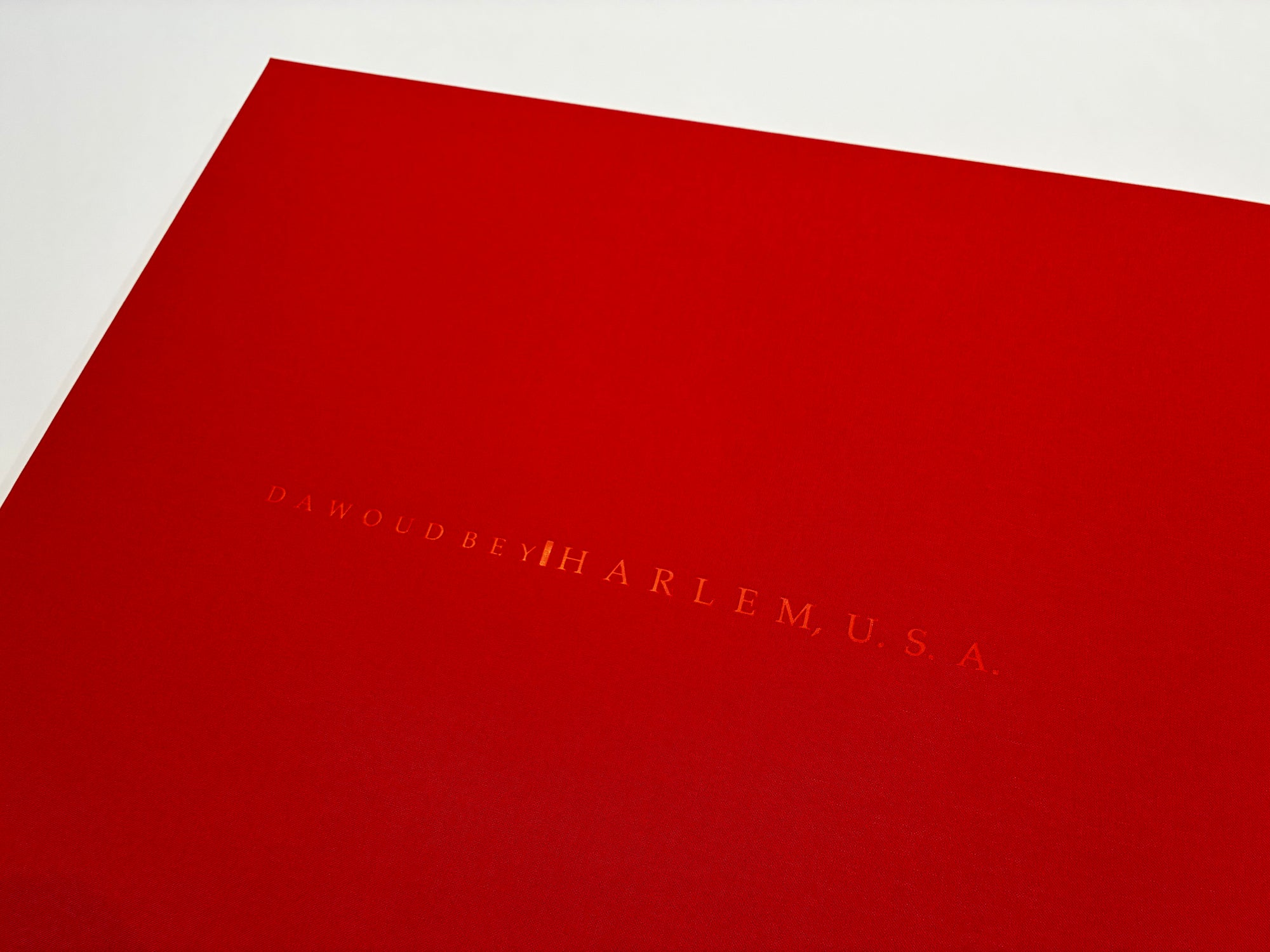 A close-up of a bright red portfolio box with embossing reading 'DAWOUD BEY | HARLEM, U.S.A."